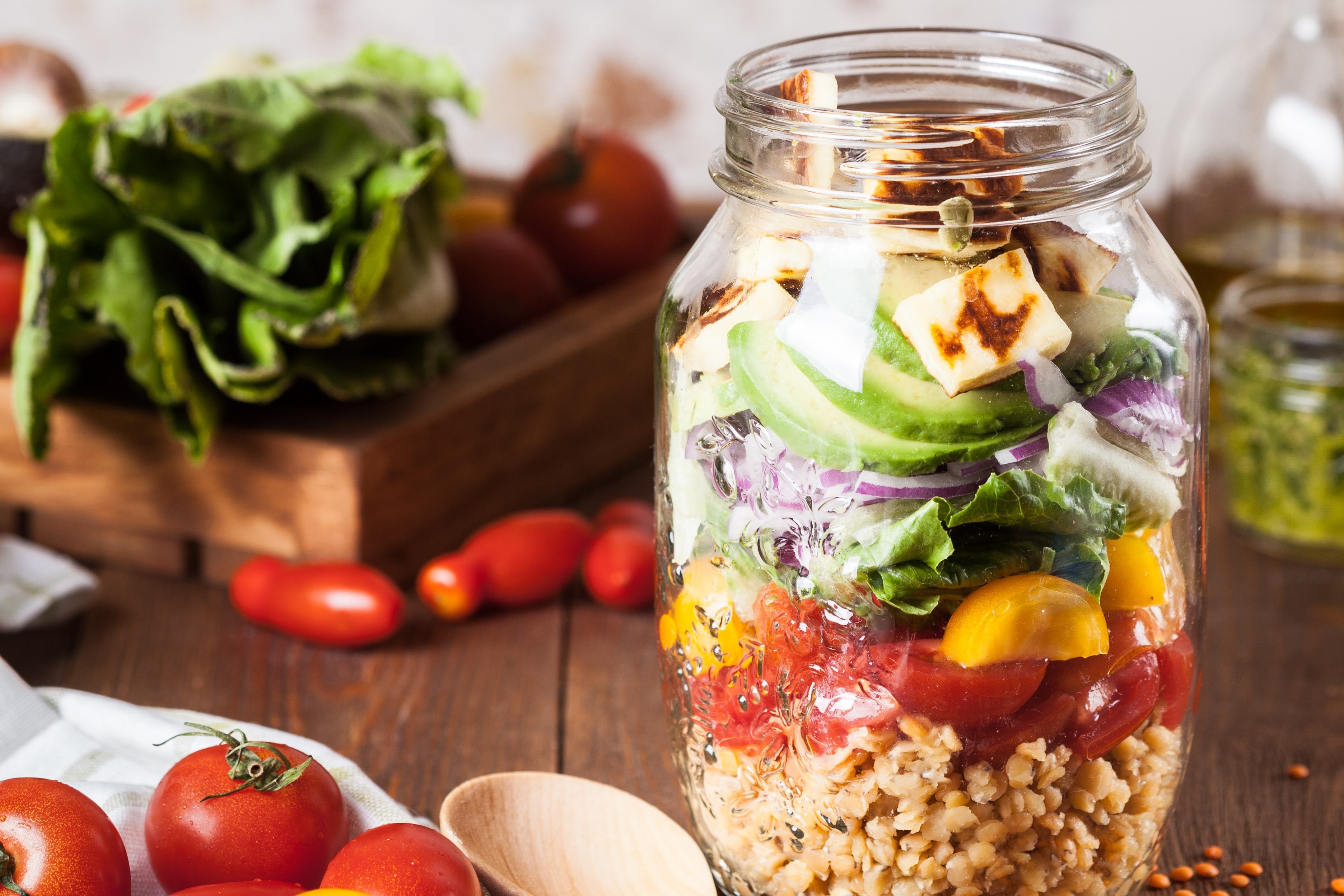 Layered mason jar salad with grains, veggies, avocado, and grilled halloumi cheese.